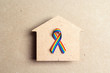 Wooden house silhouette with lgbt rainbow ribbon on brown cardboard background. Symbol of free love and tolerance to homosexual and bisexual people community.