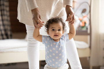Wall Mural - portrait of cute small african american baby girl learn walking at home holding mom hands, little bi