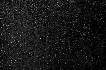 Drops of water flow down the surface of the clear glass on a black background.	