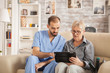 © DC Studio - Male bearded doctor in nursing home helping senior woman to use her tablet computer.