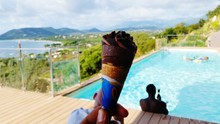Cropped Hand Holding Ice Cream Cone Against Man Relaxing In Swimming Pool