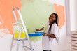 © satura_ - Young happy african american woman painting interior wall with paint roller in new house. A woman with roller applying paint on a wall.