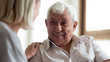 © fizkes - Happy elderly 80s man sit on couch talk have pleasant conversation with loving wife at home, caring woman touch support cheer smiling mature 70s husband, show understanding in relationships