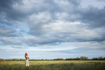 Woman stands in the middle of a green field and a blue sky with clouds