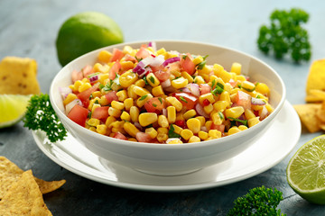 Mexican Corn Salsa in white bowl with lime and tortilla chips. Healthy food