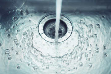 In the metal sink in the kitchen, water flows from the tap, which bubbles and flows into the drain hole.