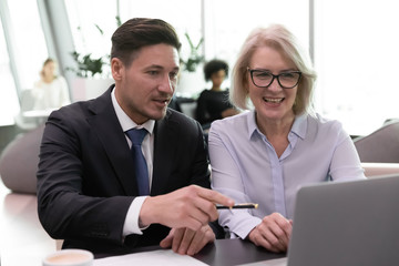 Different age colleagues sitting at desk inside of modern office hallway using computer discussing financial report datas sales increase and profits, learn new business application, teamwork concept