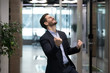 © fizkes - Millennial office worker in suit standing in hallway clenched fists feel overjoyed celebrate career advancement, got business opportunity, salary or sales growth, successful winner businessman concept