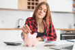 © Proxima Studio - Woman putting money into piggy bank at table