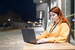 © Михаил Решетников - A woman works remotely at a laptop in a summer cafe late in the evening. A smiling girl is studying while sitting down in a wasted street at a wooden table.