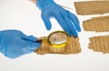 Poster - A researcher studies Arabic writing from the Koran using a magnifying glass and a table with a light. Paleography, the study of ancient Arabic writing