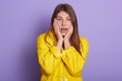 Closeup portrait of panicked female wearing casual jacket, woman keeping palms on cheeks, worried girl with opened mouth posing isolated over lilac studio background. People emotions concept.