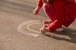 © sementsova321 - Faceless picture of little girl wearing red closing drawing colorful rainbow on asphalt road with chalk, child spending time in open air, holding piece of chalk in hands, playing in sunny day.