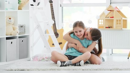 Canvas Print - Beautiful smiling sisters happily hugging on floor in kids room