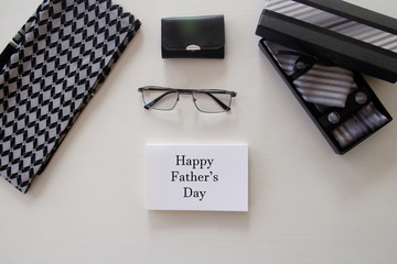 Wall Mural - Happy Father's Day inscription with tie and glases, tool kit or wallet, men's scarf, box with a tie and cufflinks with a bow on white background. Greetings and presents. white card with 
