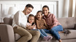 © fizkes - Happy parents with two little daughters using phone together, sitting on cozy sofa in living room, smiling father holding smartphone, preschool girls watching video online, spending weekend at home