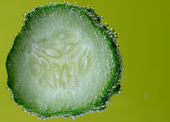 Wall Mural - Beautiful vegetable background. One slice of cucumber closeup. Texture of cucumber slices in bubbles on a yellow background.Horizontal, close-up, nobody, side view, free space. Healthy eating concept.