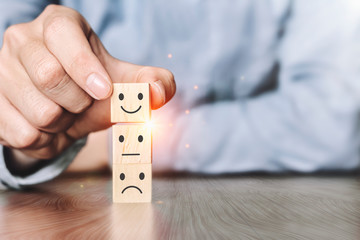 Satisfaction survey concept.Hand of a businessman Choose the feelinga smiley face on wood block cube, On the desk at the home office, The best excellent business services rating customer experience