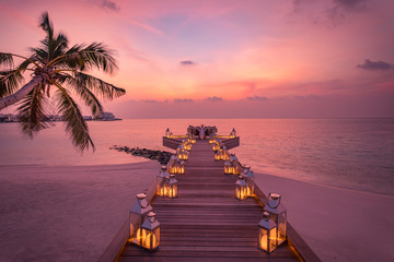 Romantic dinner on the beach with sunset, candles with palm leaves and sunset sky and sea. Amazing view, honeymoon or anniversary dinner landscape. Exotic island evening horizon, romance for a couple 