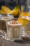 Fototapeta Do pokoju - milkshake with oatmeal, banana and orange on dark table, vertical closeup