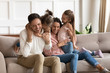 © fizkes - Happy mother and father hugging and cuddling with two little daughters, sitting on cozy sofa at home, smiling parents and preschool children having fun together, family enjoying free time