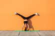 © khosrork - Overjoyed happy girl with perfect athletic body in tight sportswear doing yoga handstand pose with spread legs against wall and showing tongue, having fun. Gymnastics for body balance, flexibility