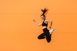 © khosrork - Happy lively vivid girl with fit body in tight sportswear jumping in air, flying and smiling full of energy, healthy sport lifestyle. studio shot, isolated on orange background, advertising area