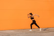 © khosrork - Motivated confident fit woman athlete in tight sportswear, black pants and top, starting to run, jogging outdoor against orange wall, advertising area. Health care and weight loss, sport activity