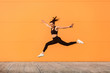 © khosrork - Positive lively vivid girl with fit body in tight sportswear jumping, running and smiling full of energy, healthy sport lifestyle. outdoor studio shot isolated on orange background, advertising area