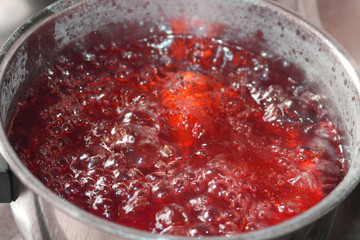 Boiling red liquid in a pot on the stove, Steam is coming up from the from the hot liquid.