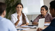 © fizkes - Attractive coach leader businesswoman with indian ethnic partner talking in boardroom at meeting. Confidence woman training diverse corporate team at briefing. Young employee share thoughts sitting.