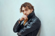 © Fxquadro - Daring and cool male model with curly hair posing in leather coat in a bright studio and leaning on the wall