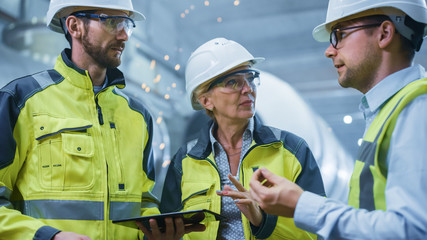 Wall Mural - Three Heavy Industry Engineers Stand in Pipe Manufacturing Factory, Use Digital Tablet Computer, Have Discussion. Large Pipe Assembled. Design and Construction of Oil, Gas and Fuels Transport Pipeline