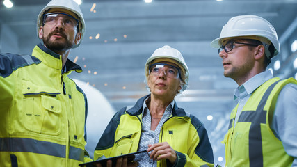 Wall Mural - Three Heavy Industry Engineers Stand in Pipe Manufacturing Factory, Use Digital Tablet Computer, Have Discussion. Large Pipe Assembly. Design and Construction of Oil, Gas and Fuels Transport Pipeline