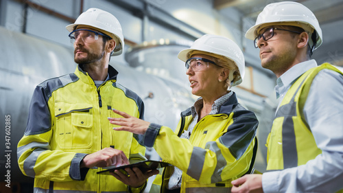 Fotomural Three Heavy Industry Engineers Stand in Pipe Manufacturing Factory, Use Digital Tablet Computer, Have Discussion