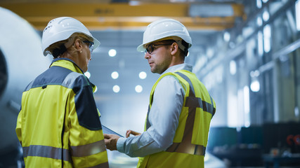 Wall Mural - Two Heavy Industry Engineers Stand in Pipe Manufacturing Factory, Use Digital Tablet Computer, Have Discussion. Construction of Oil, Gas and Fuels Transport Pipeline. Back View Sparks Flying