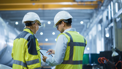 Wall Mural - Two Heavy Industry Engineers Stand in Pipe Manufacturing Factory, Use Digital Tablet Computer, Have Discussion. Large Pipe Assembled. Design and Construction of Oil, Gas and Fuels Transport Pipeline