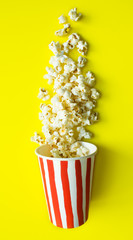 Paper Cup with drawn red stripes and scattered popcorn on a bright yellow background top view and copy space