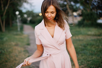 Playful young woman in pink summer dress enjoys a walk in spring park in the evening.