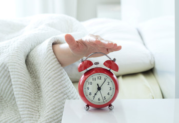 young woman sleeping on bed pressing snooze button on black vintage alarm clock at seven o'clock morning in bed room at home, lifestyle, good morning, healthy sleep and joyful weekend concept