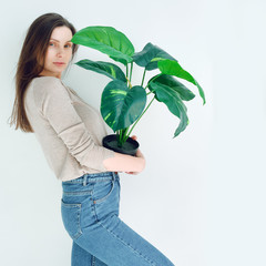 hipster girl in blue jeans with a flower pot in hand on a white background