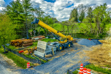 Aerial View Of Yellow Heavy Duty Jib Equipped  Telescopic Crane At A Road Widening Construction Site With Boom Nose Surrounded By Rusty Steel Pipes And Concrete Road Blocks 