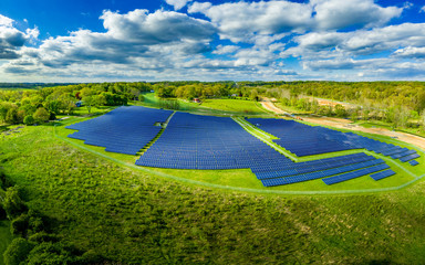 aerial view of large solar farm with hundreds of blue solar panels as the sun reflects with cloudy b
