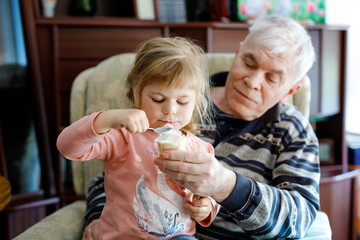 Happy grandfather and cute little toddler granddaughter, adorable child eating together ice cream. Family tasting sweet icecream, baby girl feeding senior man.