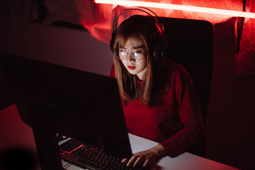 Pro player gamer young asian woman playing online video game shooting fps tournament ranking cyber internet at night red neon light room with gaming headset and keyboard on championship event.