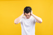 © Kiattisak - Attractive young asian man covering your ears loud noise shouting mouth angry and fury negative emotion wearing white t-shirt on yellow background isolated studio shot with copy space