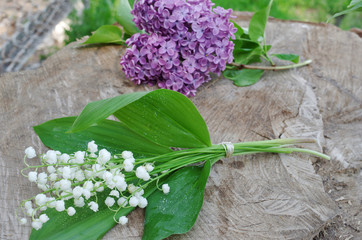 Wall Mural - A branch of lilac and a bouquet of lilies of the valley on a tree stump.