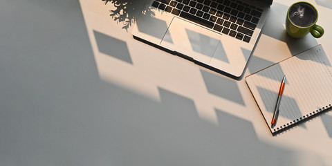 top view image of computer laptop putting on white working desk that surrounded by potted plant, cof