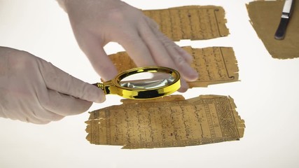 Poster - A researcher studies Arabic writing from the Koran using a magnifying glass and a table with a light. Paleography, the study of ancient Arabic writing