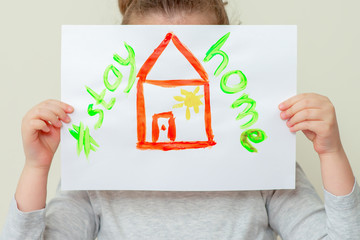 Poster - Closeup of child's hands holding a picture of red house and words Stay Home covering her face. Stay Home concept.